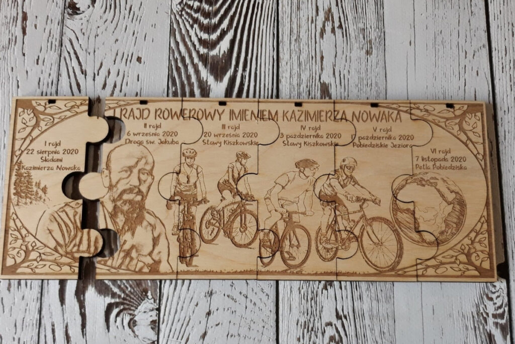 Zestaw sześciu drewnianych medali modułowych na rajd rowerowy, które po złożeniu tworzą prostokątną tabliczkę z grawerem kolarzy na trasie, logotypem wydarzenia i mapą, wykonany z jasnej brzozy bez śladów osmaleń.