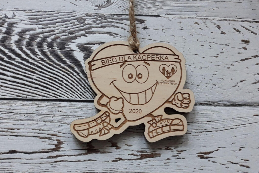 Drewniany medal na bieg charytatywny z grawerem „Biegnącego Serca” w butach sportowych, napisem „Bieg dla Kacperka” oraz miejscem na logo fundacji, wykonany z czystej brzozy bez śladów dymu.sklejki brzozowej.