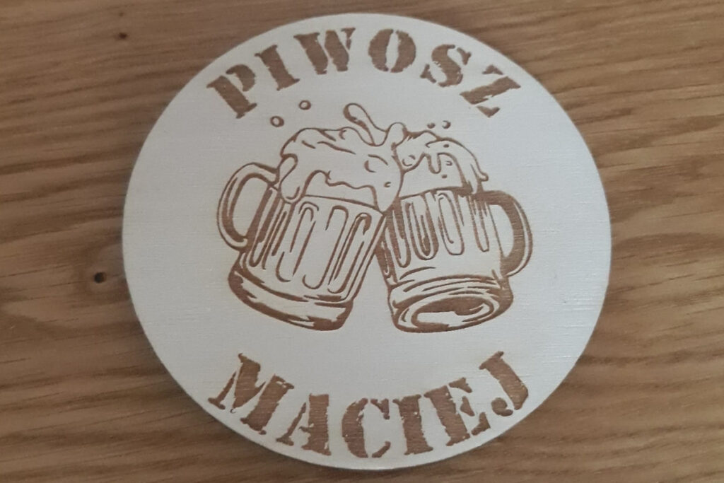 Okrągła drewniana podstawka pod kufel z grawerem „Piwosz Maciej”, grafiką pienistego kufla piwa, wykonana z jasnej sklejki brzozowej bez śladów dymu i osmaleń.