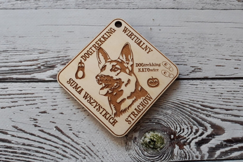 Trapezowy drewniany medal na zawody dogtrekkingowe, z grawerem głowy psa oraz nazwą wydarzenia, wykonany z czystej brzozy bez śladów dymu i osmaleń.