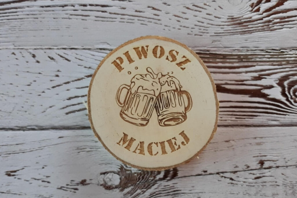 Okrągła drewniana podstawka pod kufel z grawerem „Piwosz Maciej”, grafiką pienistego kufla piwa, wykonana z jasnej sklejki brzozowej bez śladów dymu i osmaleń.