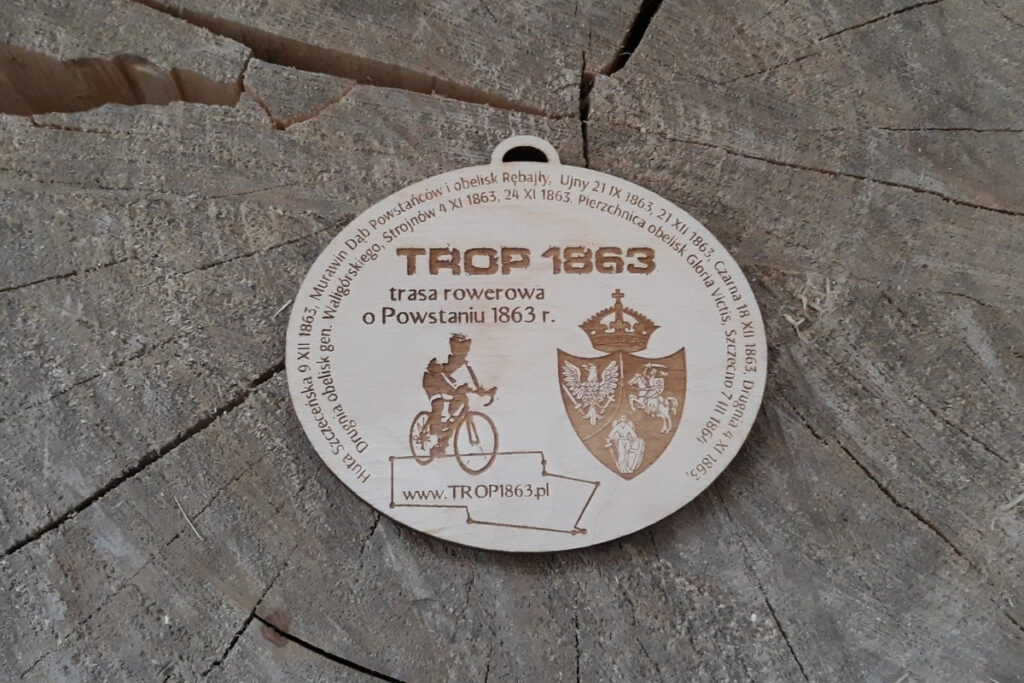 Owalny drewniany medal na rajd rowerowy z motywem historycznym, przedstawiający grawer postaci rowerzysty oraz pamiątkową inskrypcję, wykonany z czystej brzozy bez osmaleń.