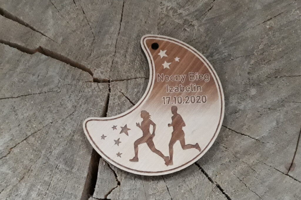 Drewniany medal w kształcie półksiężyca na „Nocny Bieg”, z grawerem rozgwieżdżonego nieba, sylwetką biegacza oraz nazwą wydarzenia, wykonany z jasnej brzozy bez śladów dymu i osmaleń.
