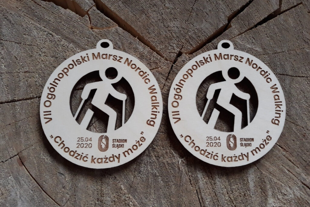 Okrągły drewniany medal na Ogólnopolski Rajd Nordic Walking „Chodzić każdy może”, z ażurowo wyciętą sylwetką osoby maszerującej z kijkami oraz grawerem logotypu wydarzenia, wykonany z czystej brzozy bez śladów dymu.