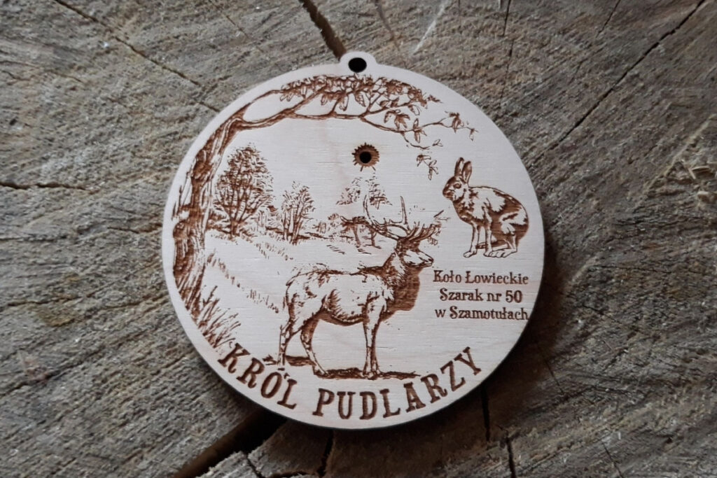 Drewniany medal na sklejce brzozy, przedstawiający grawer  jelenia byka oraz napis „Król Pudlarzy”, wykonany w rustykalnym, naturalnym stylu.