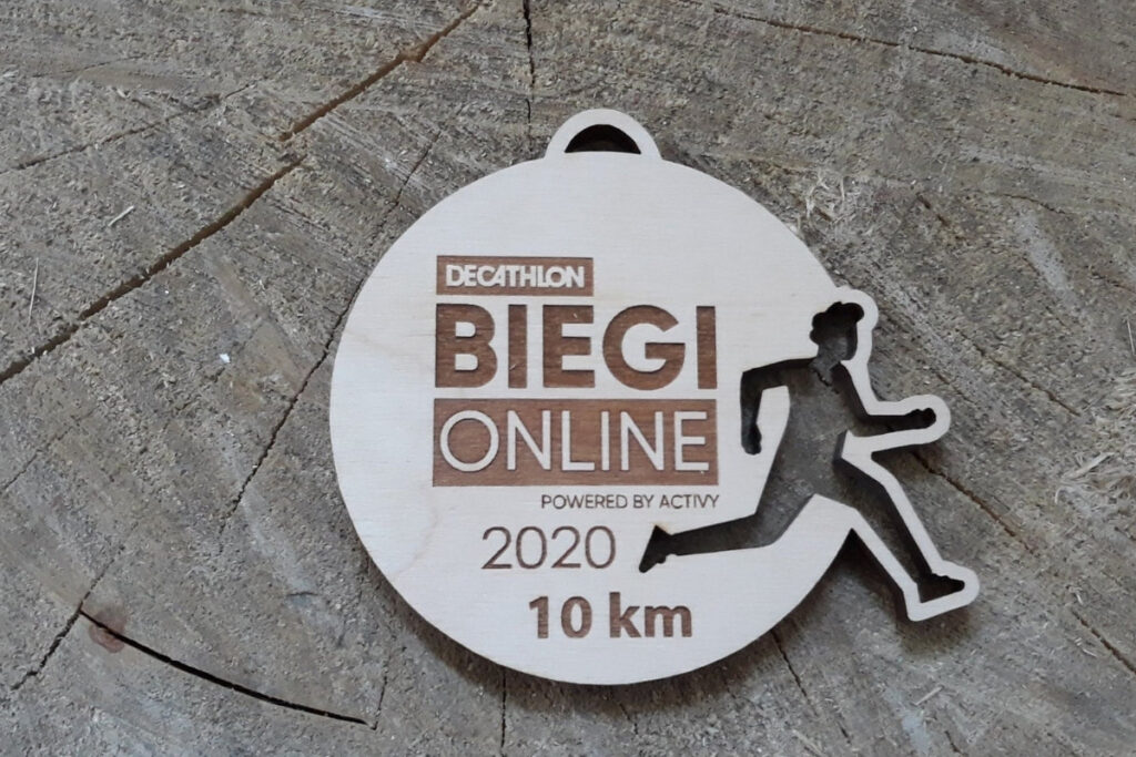 Ażurowy drewniany medal z wyciętą sylwetką biegacza, przygotowany na biegi online w formie ekologicznej pamiątki.