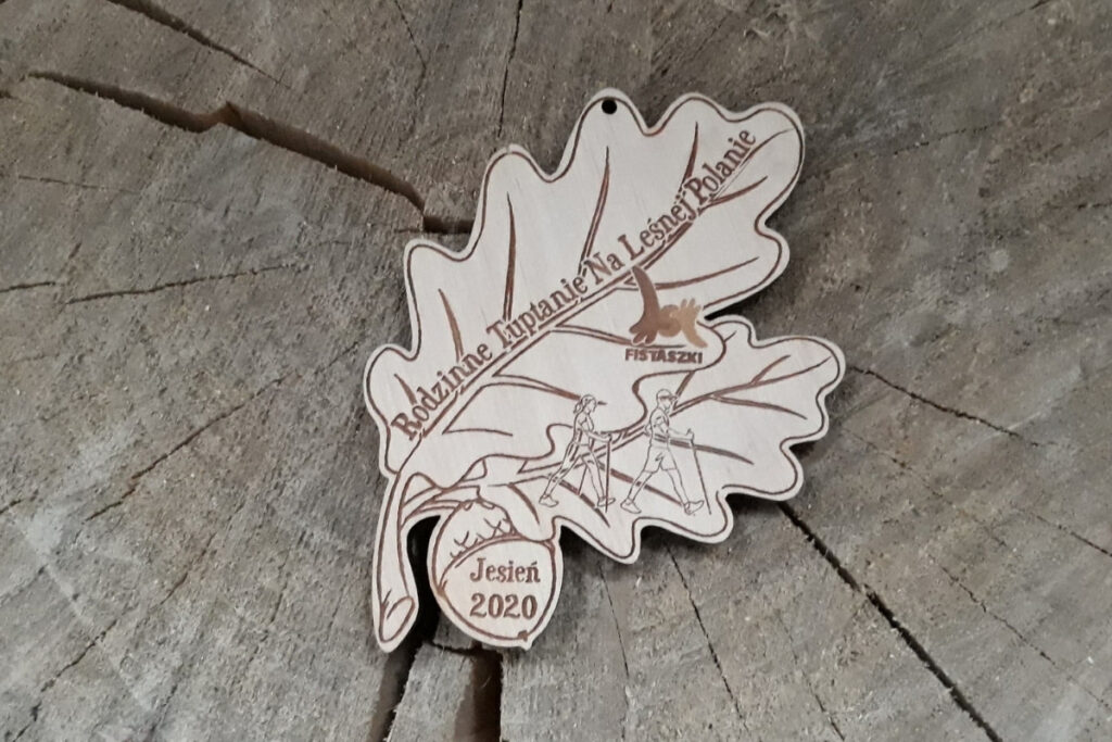 Ekologiczny drewniany medal w kształcie liścia dębu z grawerowaną szyszką, przygotowany na wydarzenie Rodzinne Tuptanie.