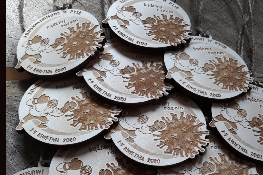 Okrągły drewniany medal z grawerem cząsteczki wirusa z napisem „Koronawirusowi w pysk!”, upamiętniający sportową wytrwałość w dobie pandemii, wykonany z czystej brzozy bez śladów osmaleń.