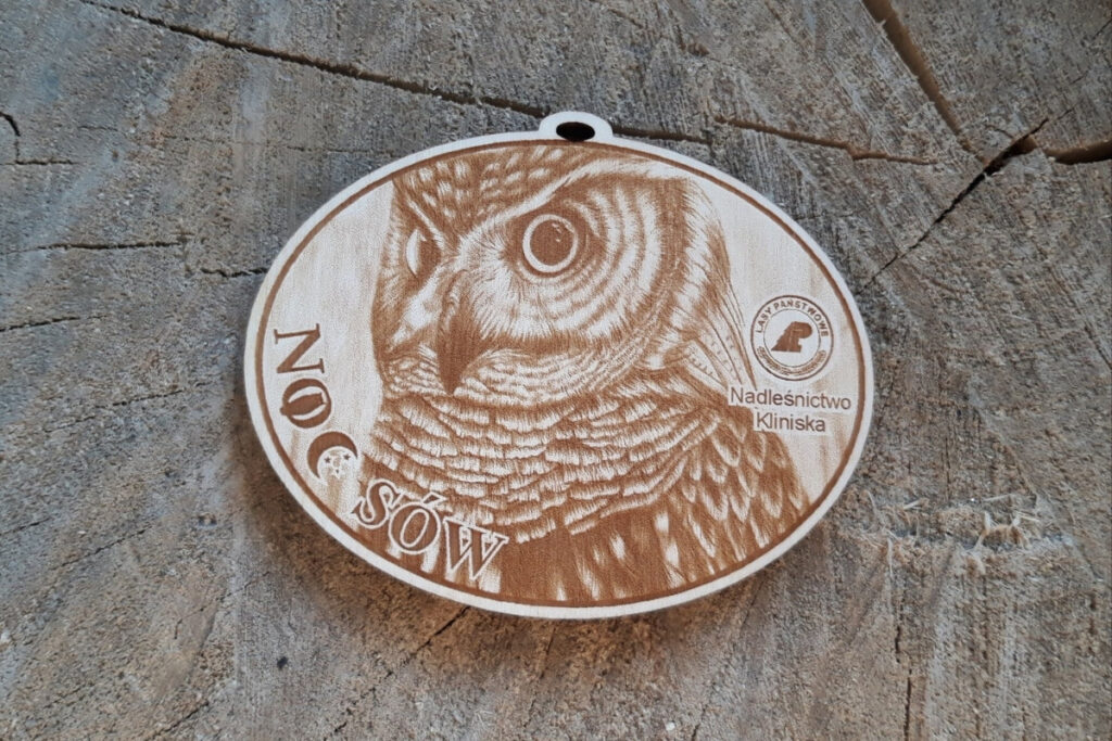 Okrągły drewniany medal na wydarzenie „Noc Sów” z bardzo szczegółowym grawerem portretu sowy.